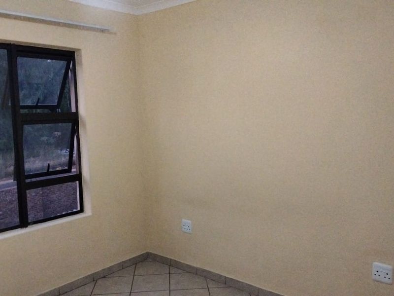 A clean, empty bedroom featuring neutral painted walls, tiled flooring, and a modern aluminium-framed window.
