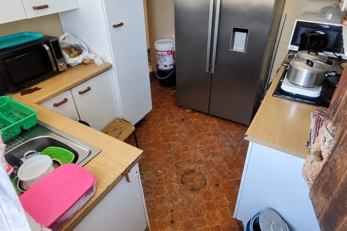 A compact kitchen featuring laminate countertops, built-in cabinetry, and a stainless steel sink, currently showing significant wear and tear on the flooring and cabinetry.