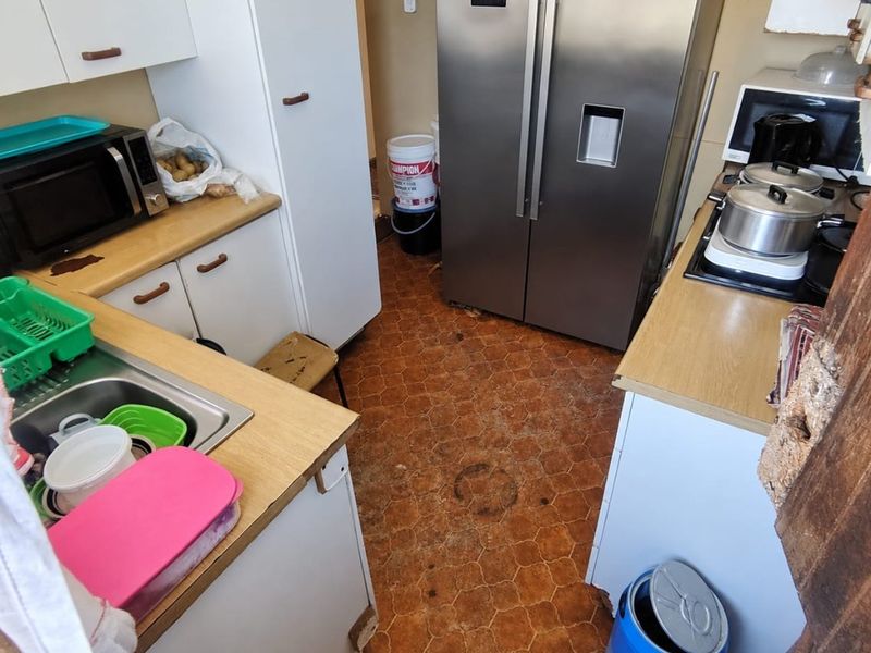 A compact kitchen featuring laminate countertops, built-in cabinetry, and a stainless steel sink, currently showing significant wear and tear on the flooring and cabinetry.