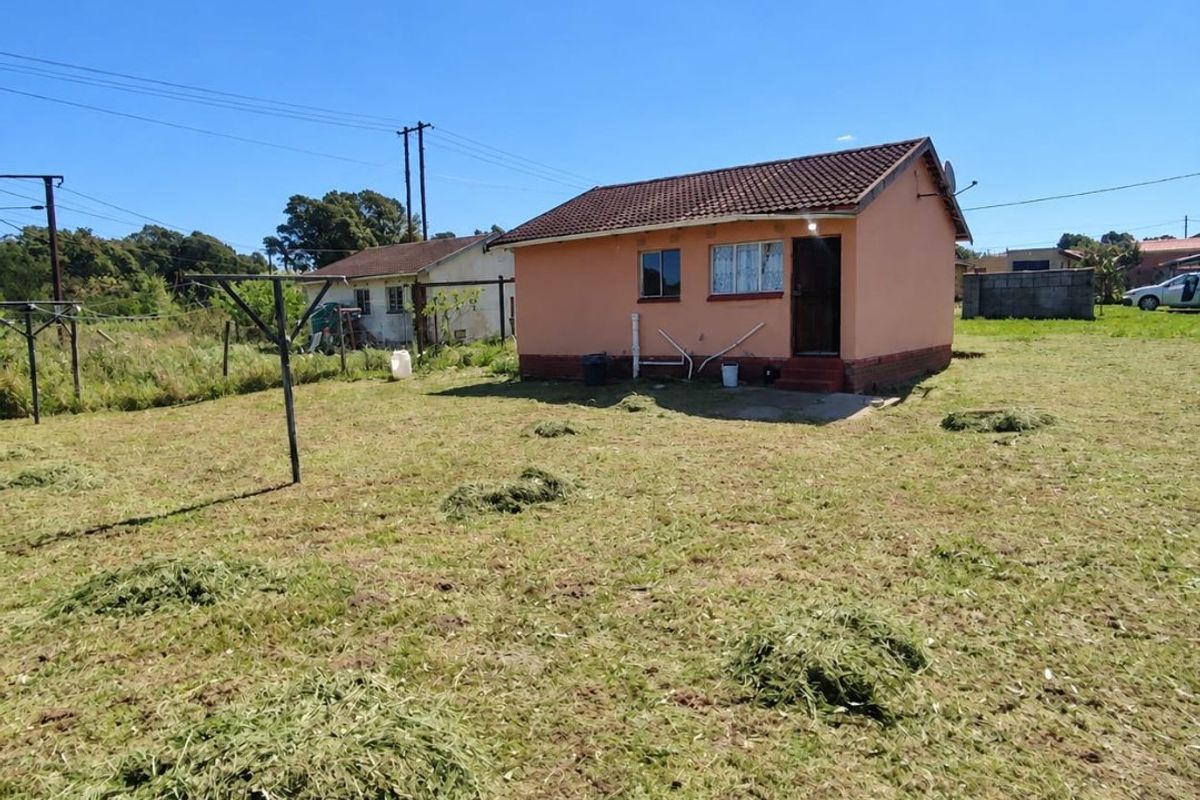 Rear view of a detached single-story house with a tiled roof and plastered exterior walls, situated on a large open plot.