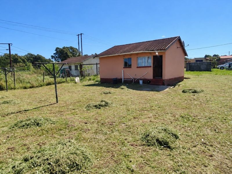Rear view of a detached single-story house with a tiled roof and plastered exterior walls, situated on a large open plot.