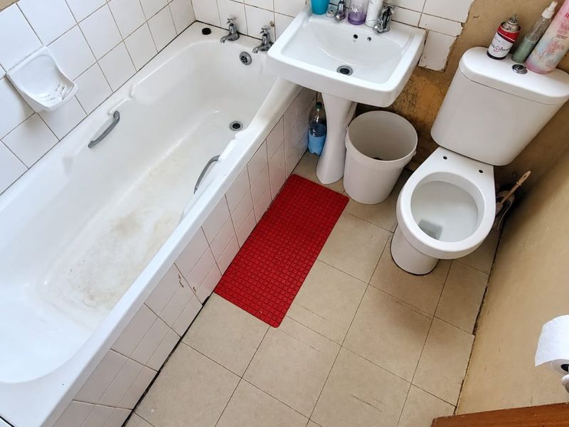 A compact bathroom featuring a standard bathtub, pedestal basin, and toilet with tiled finishes, currently requiring renovation and cosmetic updates.