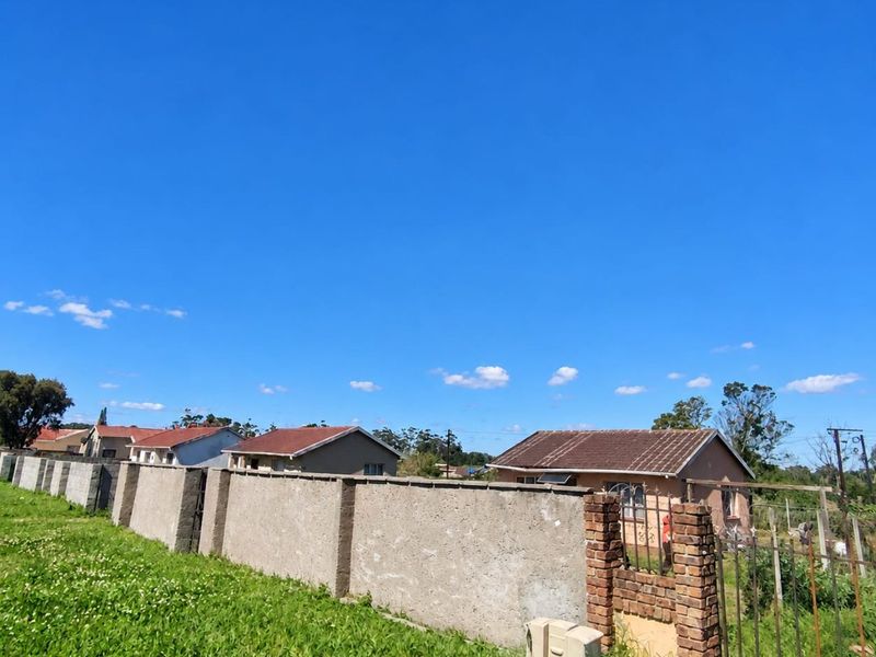A street-level view of a residential property featuring a perimeter boundary wall, brick entrance pillar, and metal gate under a clear blue sky.
