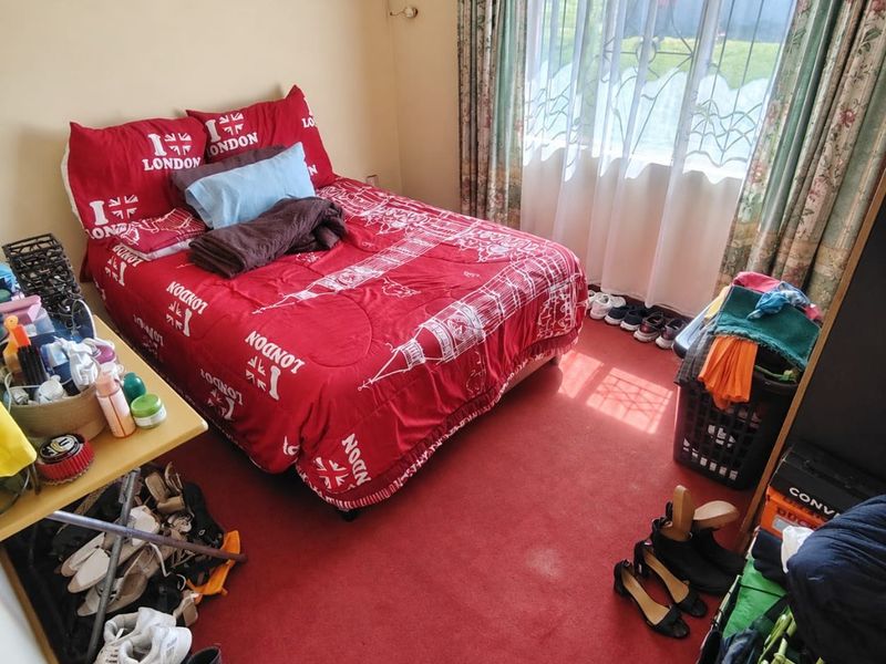 A bedroom featuring red carpet flooring, a window with security gate, and curtain rails, offering a functional space for rest.
