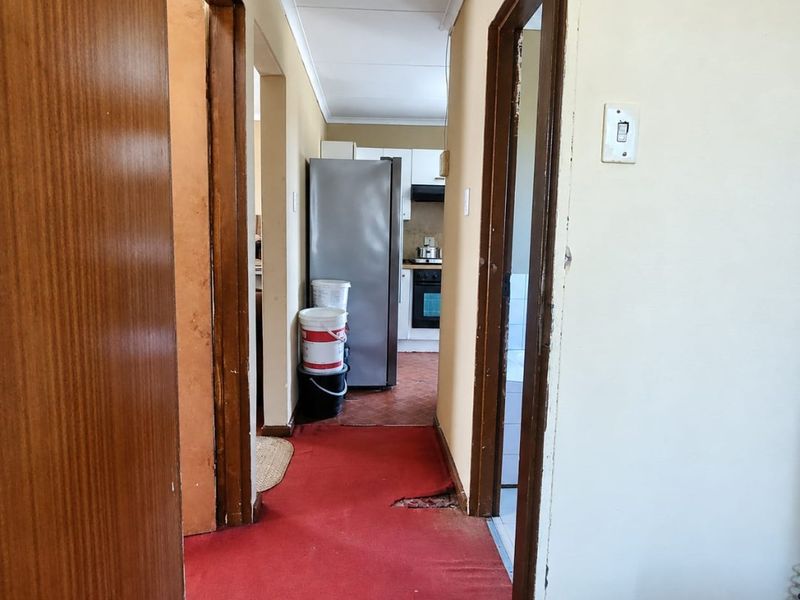 A narrow hallway with worn red carpeting, wooden door frames, and access to adjacent rooms and the kitchen area.