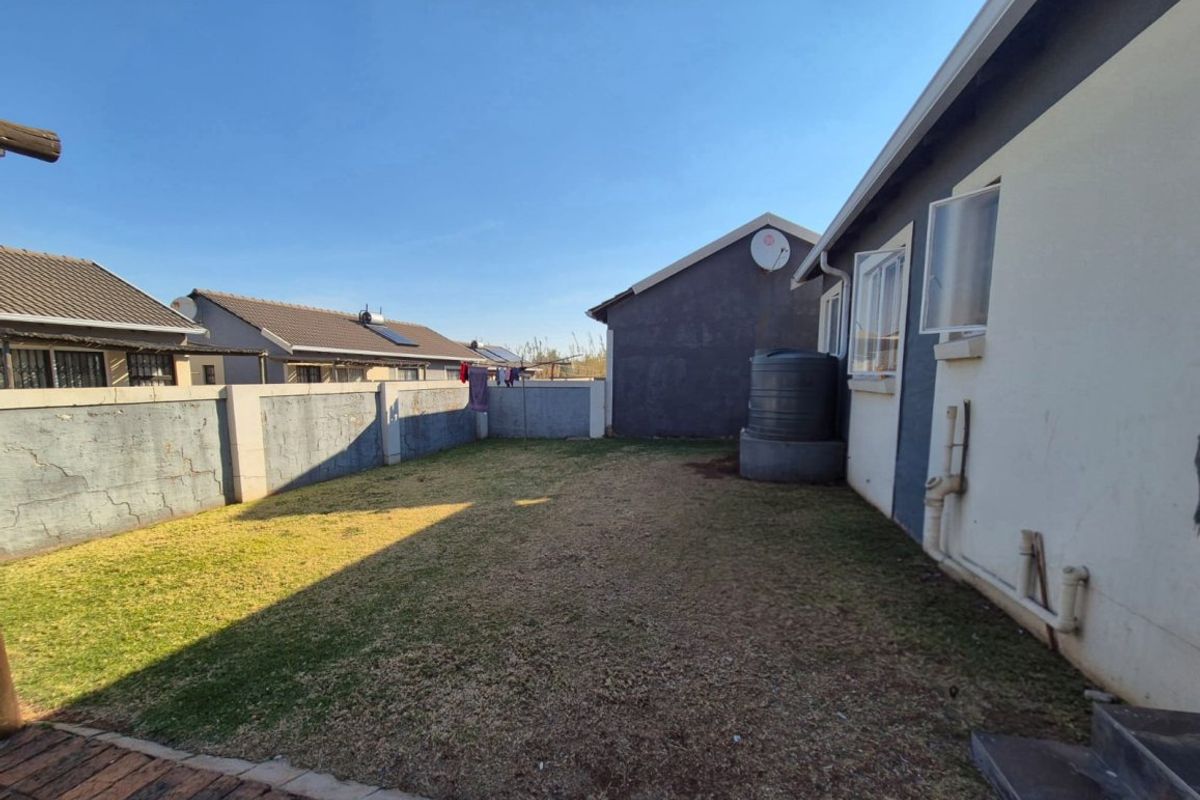 A view of the rear garden featuring a lawn, perimeter wall with visible cracking, and an external water tank attached to the house structure.