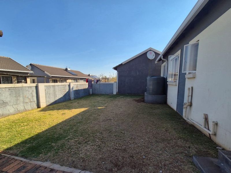 A view of the rear garden featuring a lawn, perimeter wall with visible cracking, and an external water tank attached to the house structure.