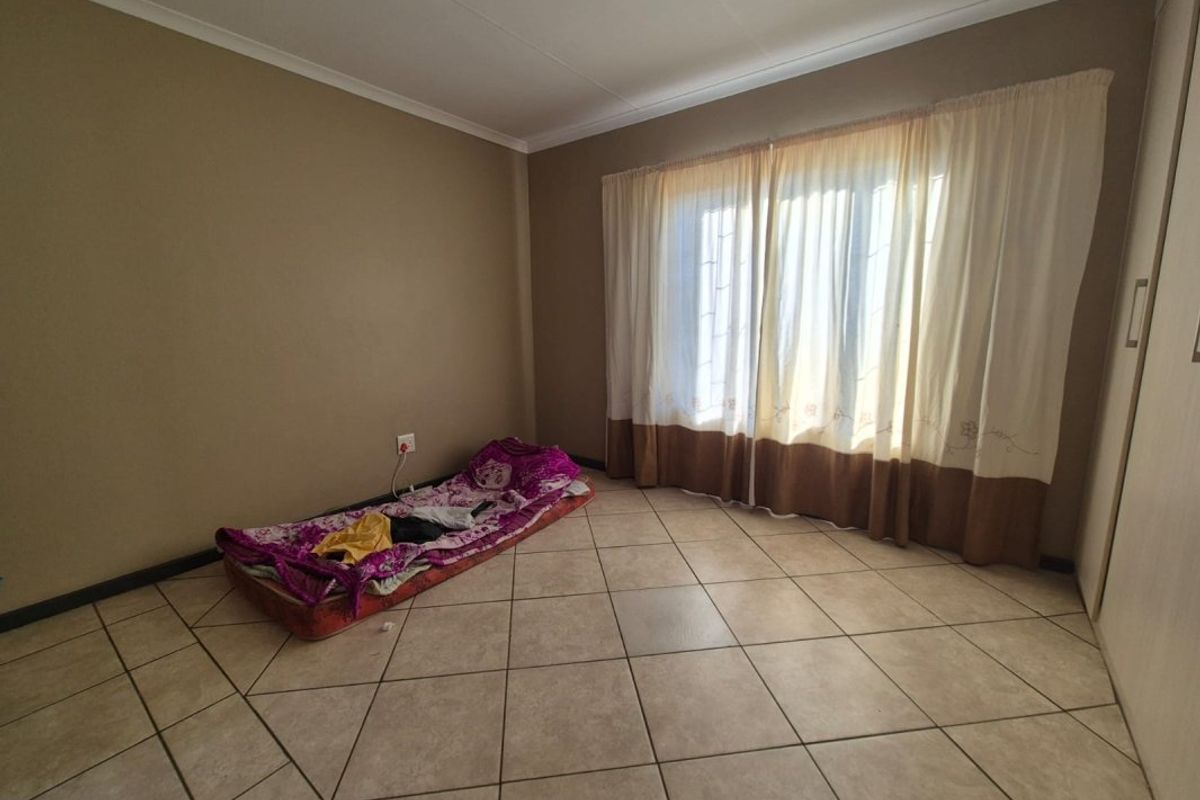 A spacious bedroom featuring neutral wall tones, tiled flooring, and built-in cupboards, offering a clean and functional space ready for personalization.