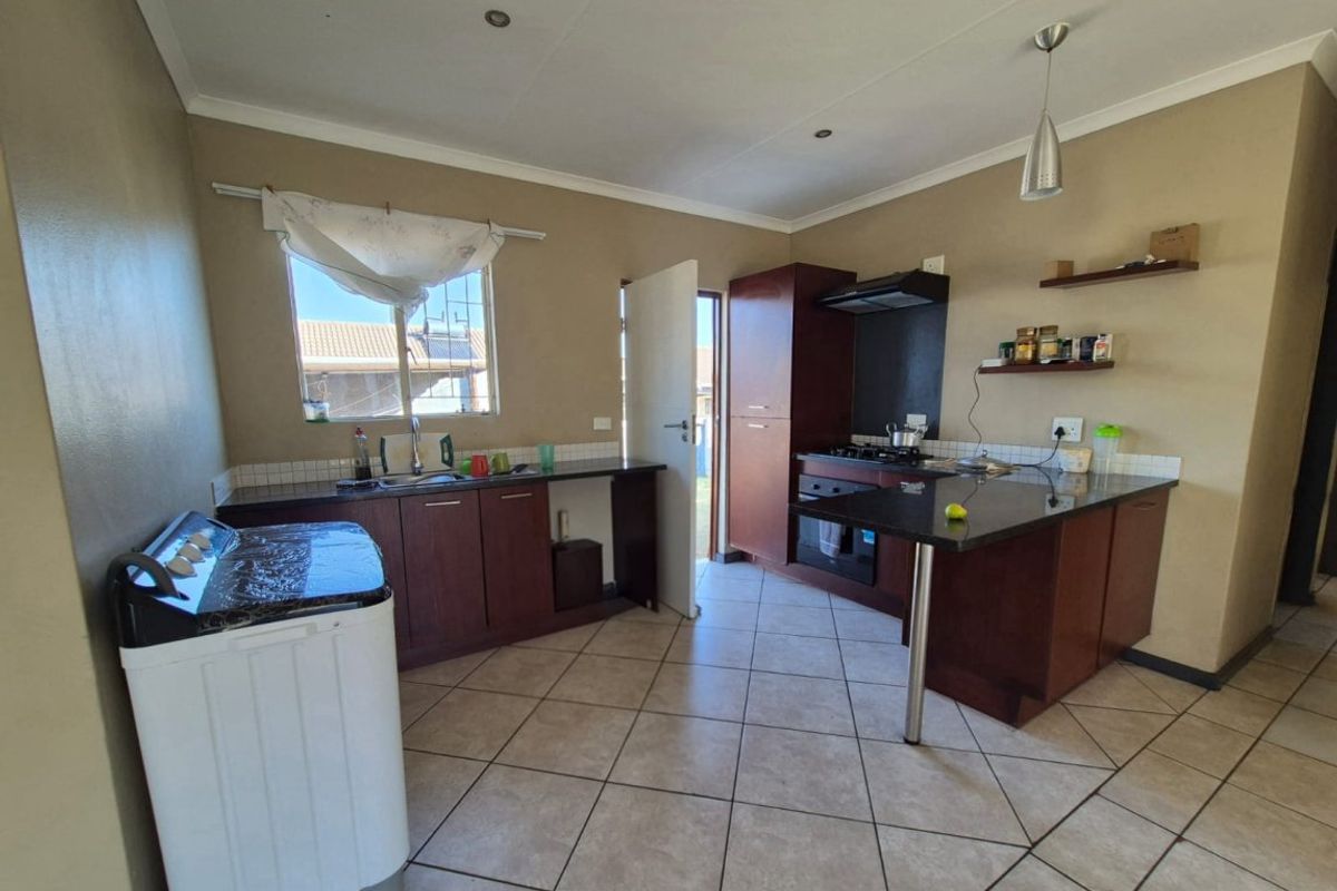 Functional kitchen featuring dark wood cabinetry, granite countertops, built-in oven, gas hob, extractor fan, and tiled flooring with direct outdoor access.