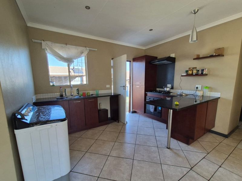 Functional kitchen featuring dark wood cabinetry, granite countertops, built-in oven, gas hob, extractor fan, and tiled flooring with direct outdoor access.