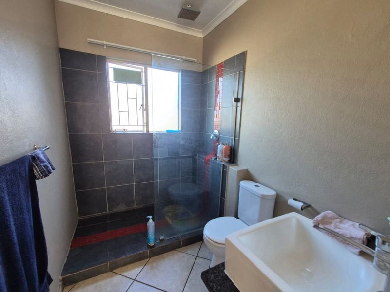 A functional bathroom featuring a walk-in shower with glass screen, a standard toilet, and a vanity basin with tiled finishes.