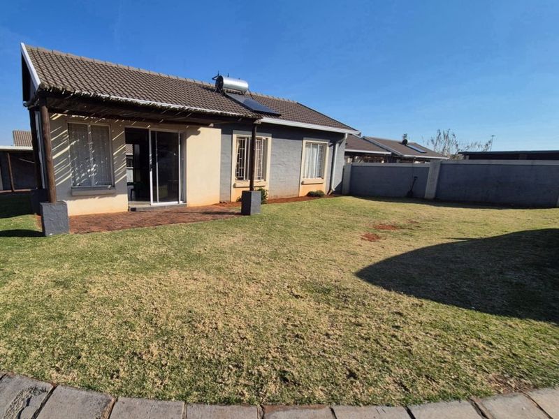 Rear view of the house featuring a covered patio, solar water heater, and a private garden enclosed by a perimeter wall.