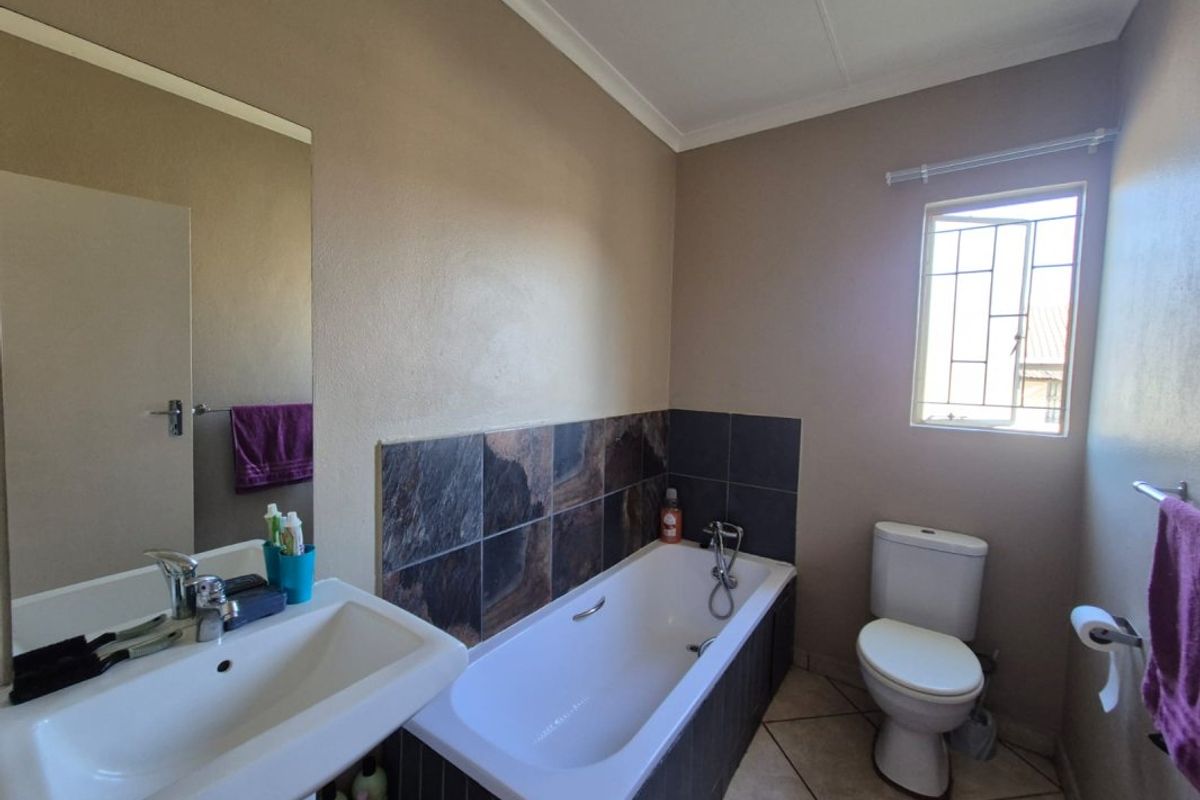 A functional bathroom featuring a built-in bathtub with tiled splashback, a wall-mounted basin, and a standard toilet with tiled flooring.