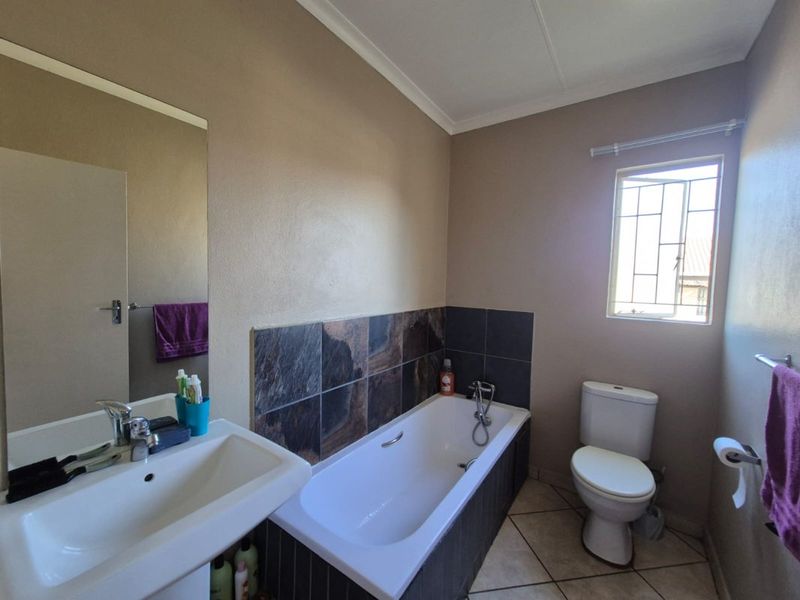 A functional bathroom featuring a built-in bathtub with tiled splashback, a wall-mounted basin, and a standard toilet with tiled flooring.