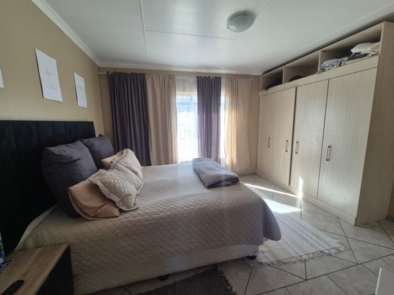 A well-maintained bedroom featuring neutral wall tones, tiled flooring, and extensive built-in cupboard storage.