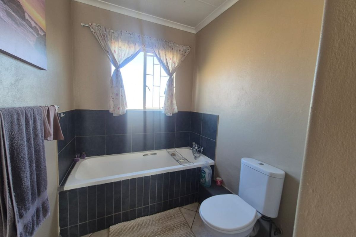 A functional bathroom featuring a built-in bathtub with dark tiled surround, a standard toilet, and tiled flooring.