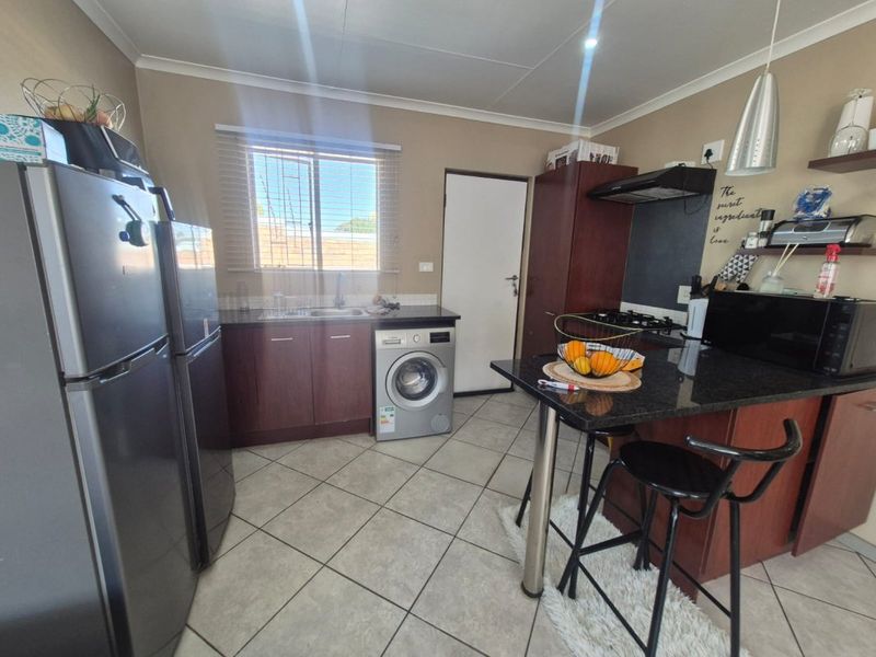 A functional kitchen featuring dark wood cabinetry, granite countertops, a gas hob with extractor, and integrated space for a washing machine.