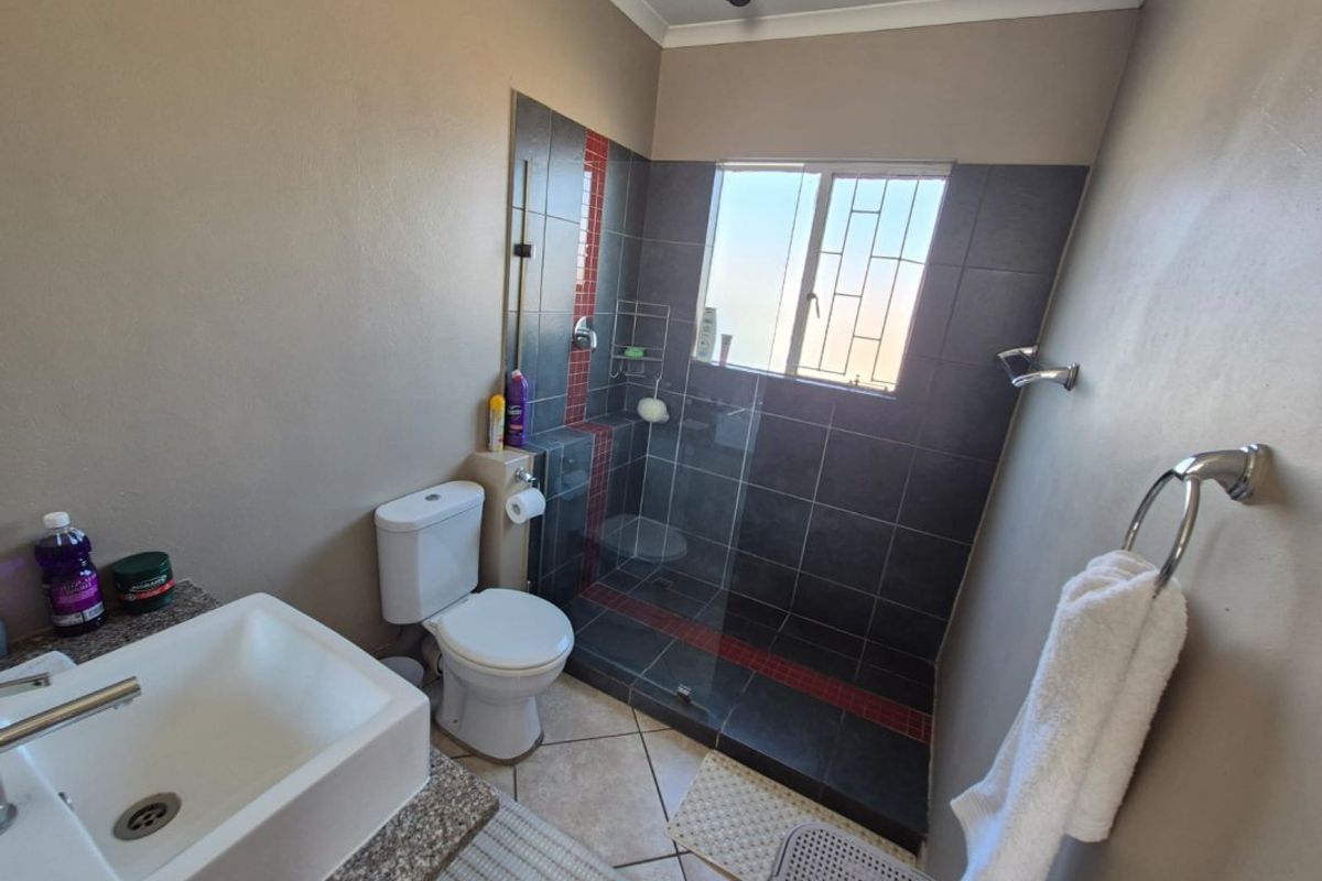 A functional bathroom featuring a walk-in shower with dark tiling, a modern vessel sink on a granite vanity, and a standard toilet.