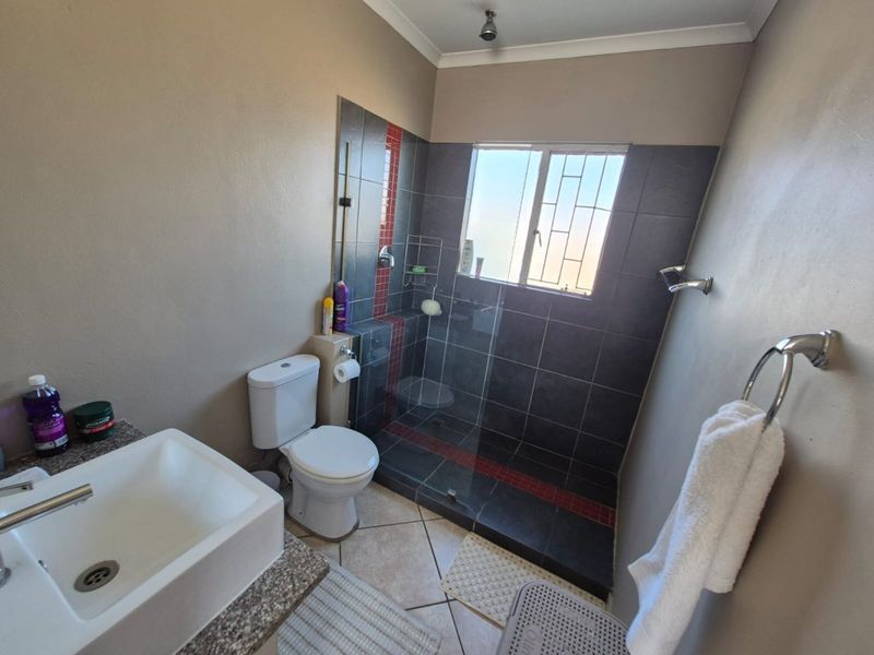 A functional bathroom featuring a walk-in shower with dark tiling, a modern vessel sink on a granite vanity, and a standard toilet.