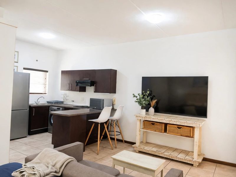 Open-plan living area featuring a functional kitchen with dark wood cabinetry, breakfast bar, and tiled flooring throughout the combined space.