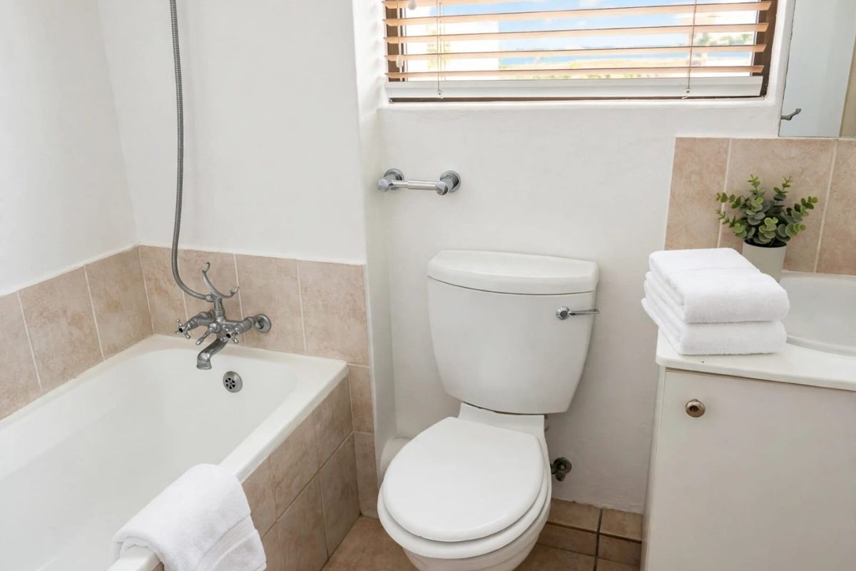 A functional bathroom featuring a bathtub with shower mixer, a standard toilet, and a vanity cabinet with an integrated basin and tiled splashback.