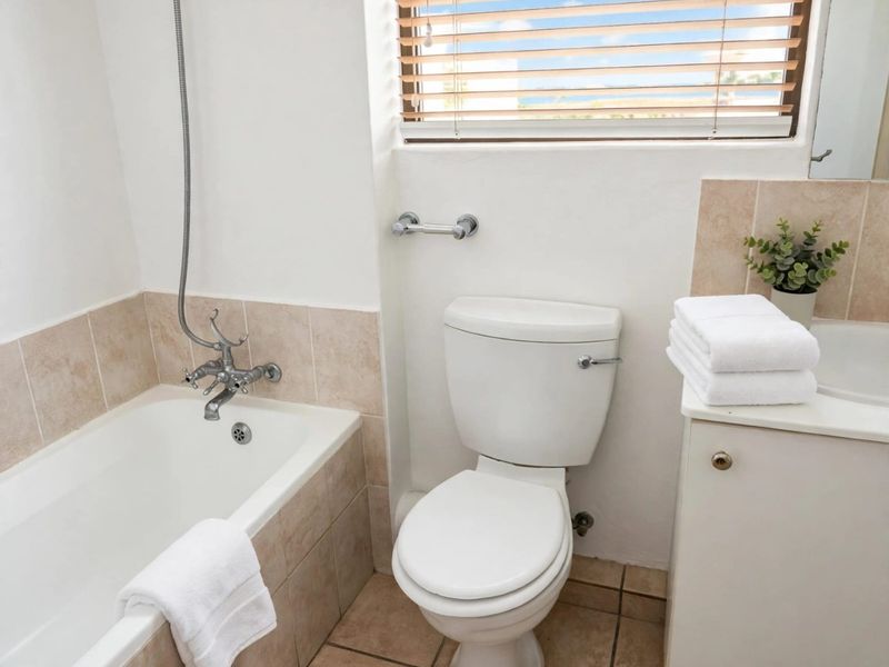 A functional bathroom featuring a bathtub with shower mixer, a standard toilet, and a vanity cabinet with an integrated basin and tiled splashback.
