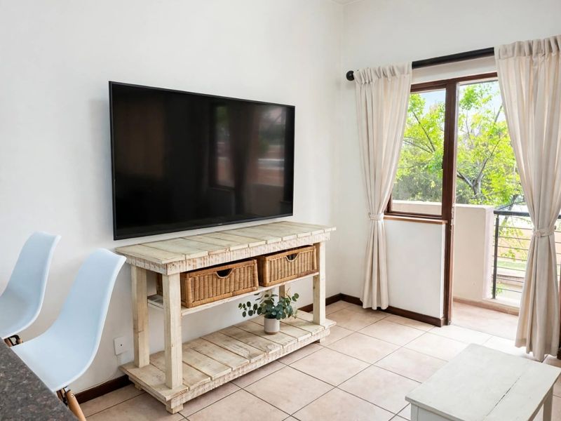 A bright living room featuring tiled flooring and a sliding glass door providing access to an outdoor balcony area.