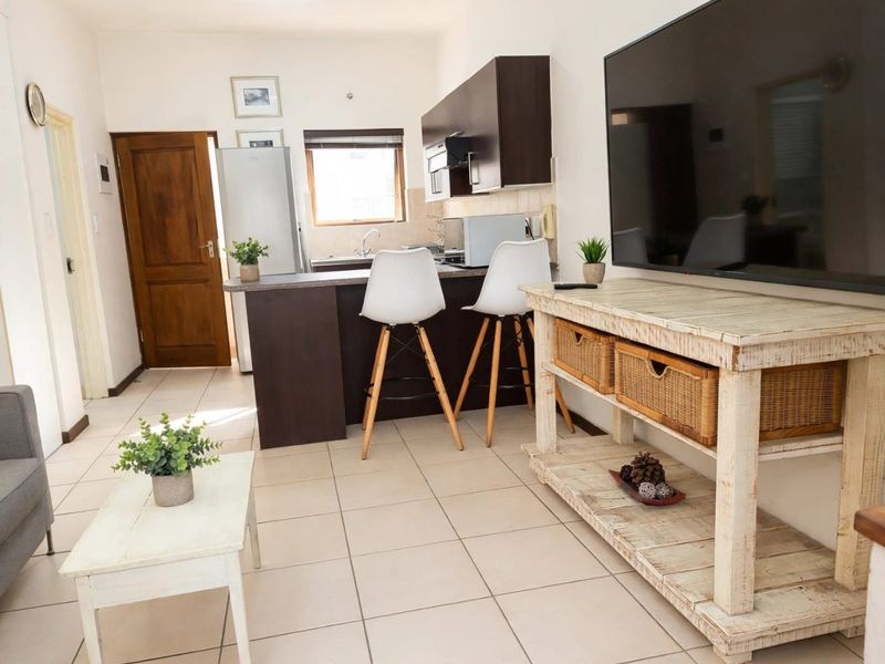 Open plan living area featuring tiled flooring and a compact kitchen with dark cabinetry and a breakfast counter.