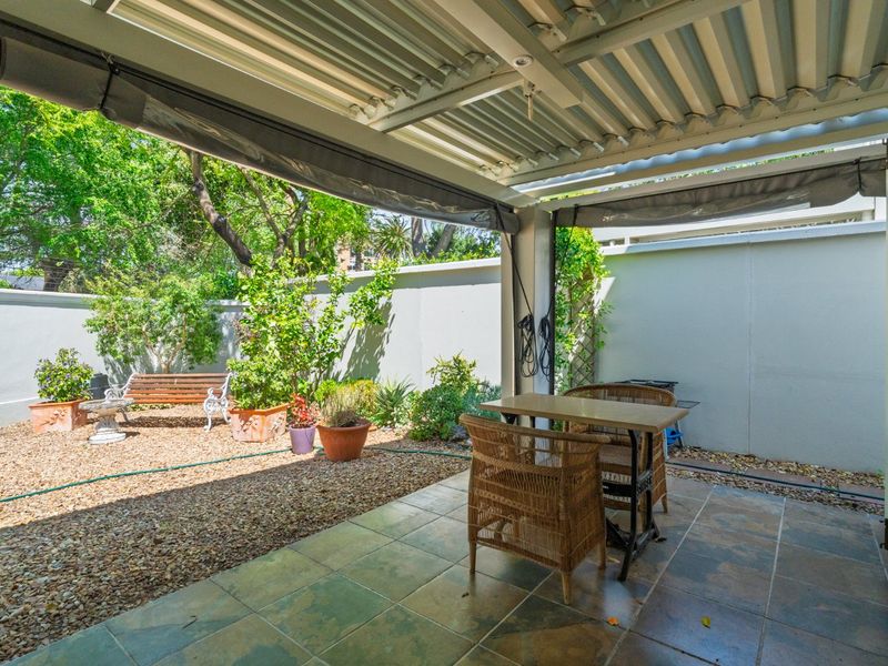 A covered patio area featuring tiled flooring, a corrugated metal roof, and a retractable shade awning, overlooking a low-maintenance gravel garden.