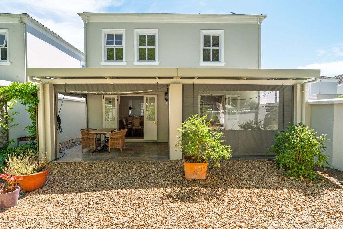 Rear view of the property featuring a covered patio with tiled flooring, retractable outdoor blinds, and a low-maintenance gravel garden area.