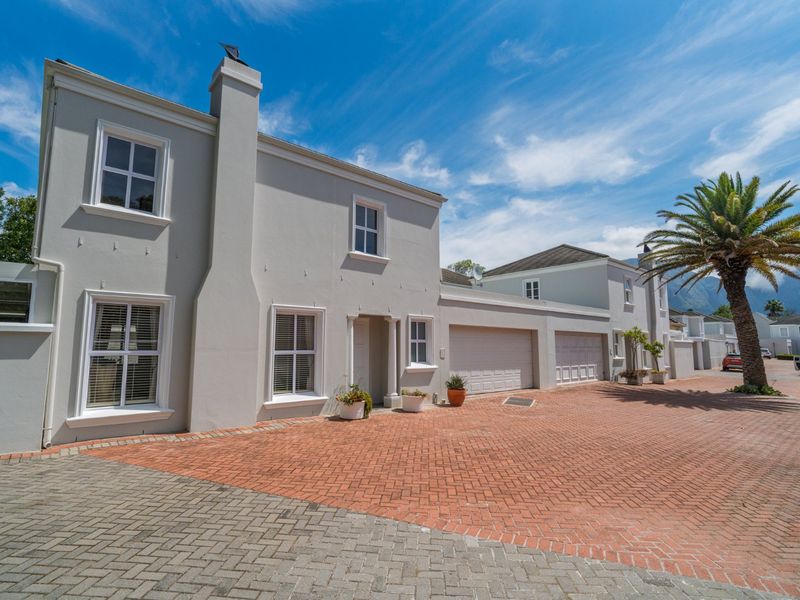 A well-maintained double-story residential property featuring a brick-paved driveway, double garage, and classic architectural detailing under a clear blue sky.