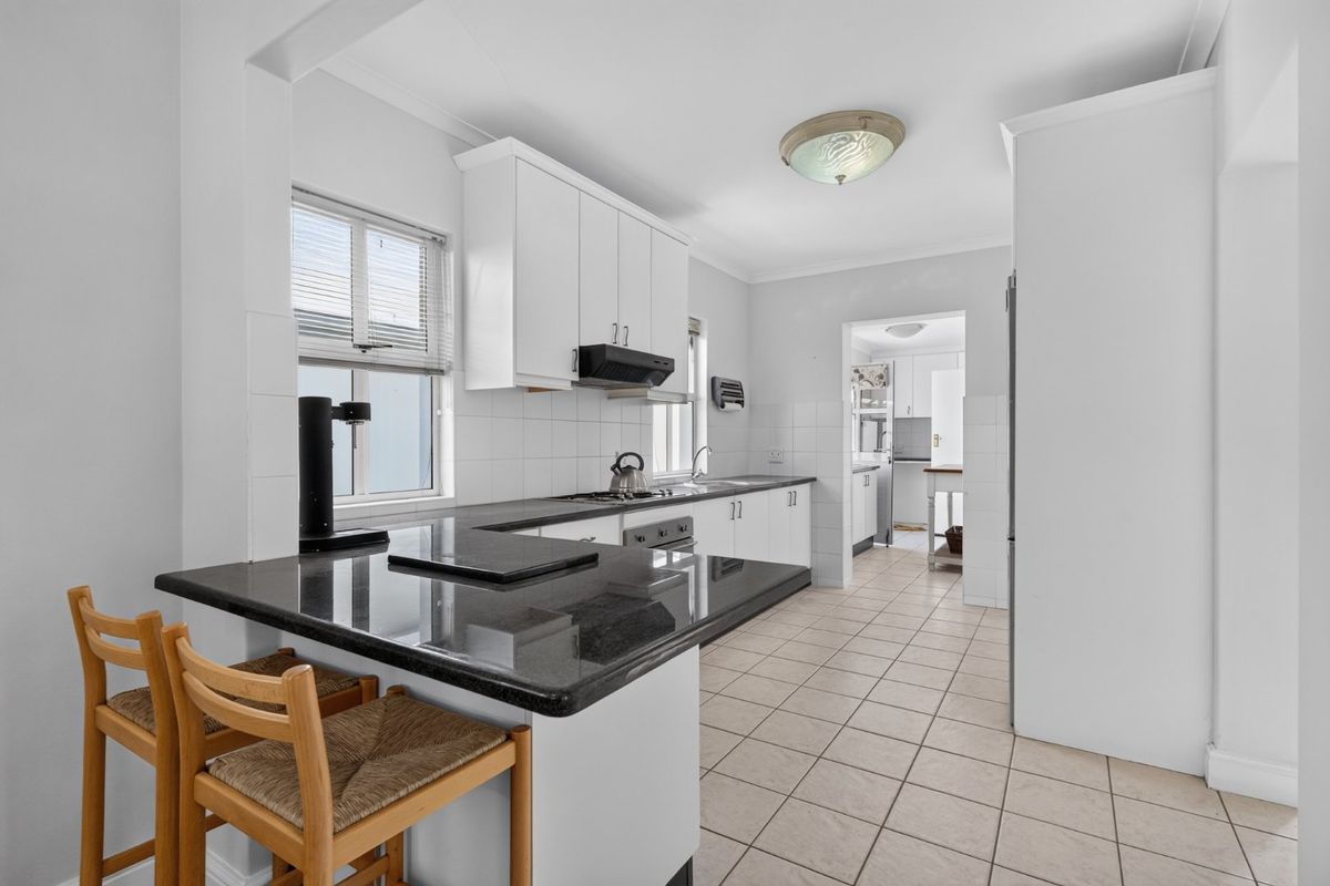 A functional kitchen featuring white cabinetry, dark granite countertops, tiled flooring, and a breakfast bar, with an adjoining scullery area visible.