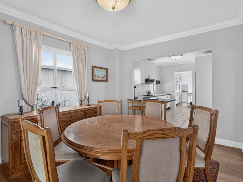 Open plan dining area flowing into a functional kitchen with white cabinetry and tiled flooring, featuring classic crown molding and hardwood floors.