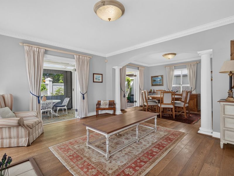 Spacious open-plan living and dining area featuring hardwood flooring, elegant crown molding, and decorative columns leading to an outdoor patio space.