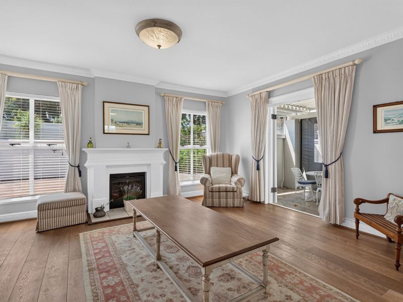 A bright and inviting living room featuring hardwood flooring, a classic fireplace with a mantel, and double doors leading to an outdoor patio area.
