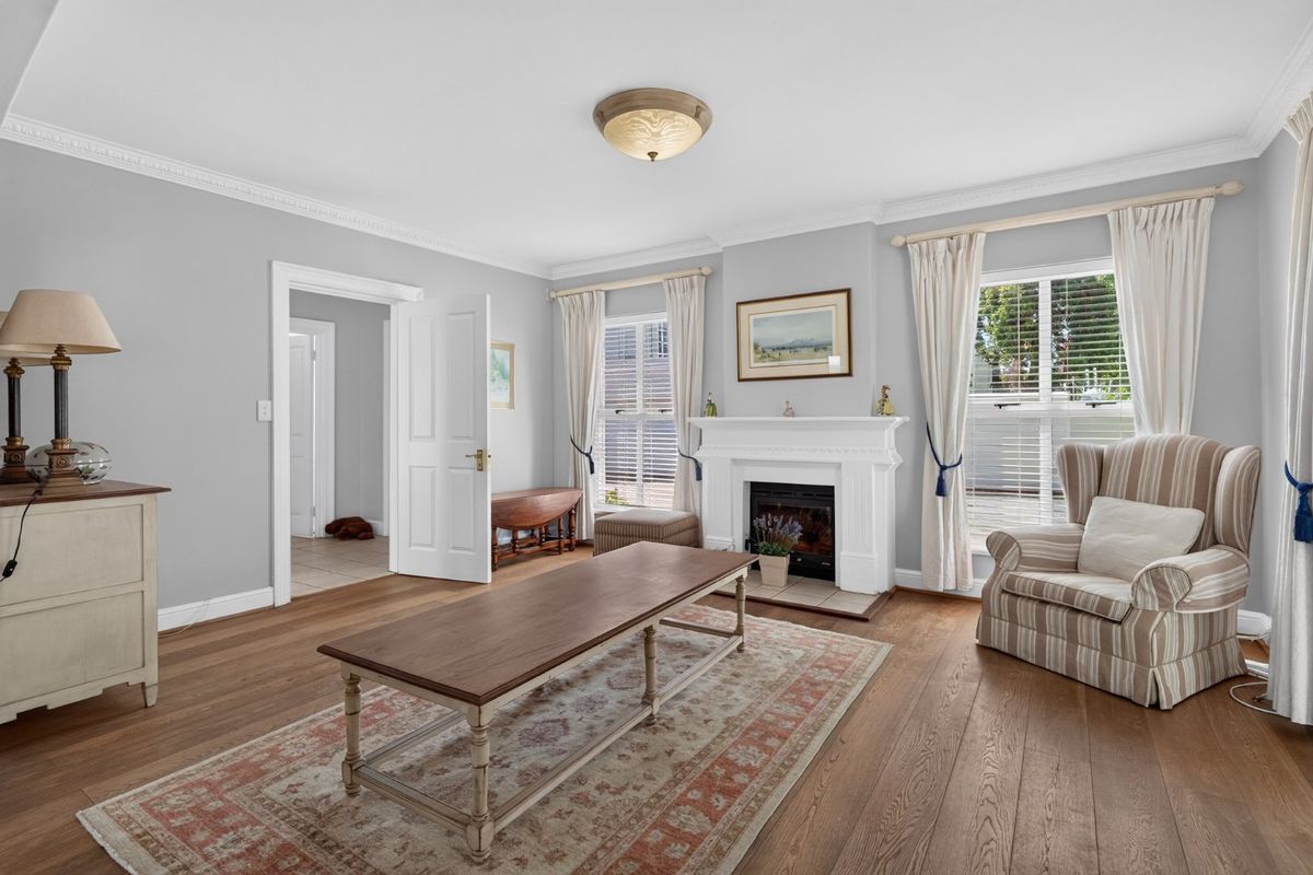 A bright and well-maintained living room featuring hardwood flooring, crown molding, and a classic fireplace with a decorative mantelpiece.