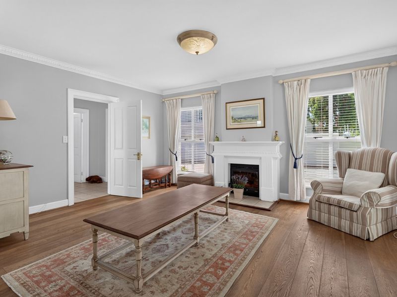 A bright and well-maintained living room featuring hardwood flooring, crown molding, and a classic fireplace with a decorative mantelpiece.