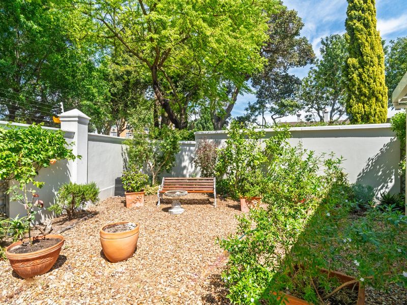 A private, low-maintenance garden area featuring gravel landscaping, mature trees, and a solid boundary wall for added privacy.