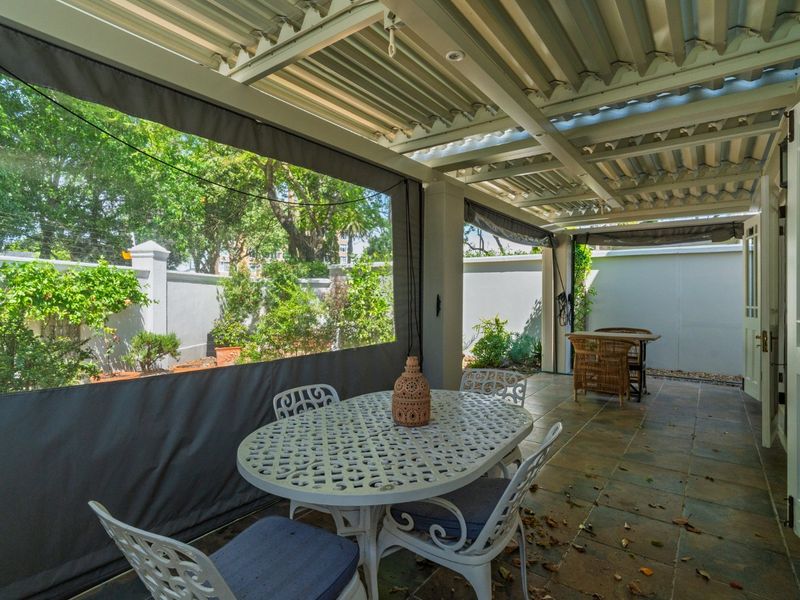 A covered patio area featuring tiled flooring, a corrugated metal roof, and retractable outdoor blinds, providing a sheltered space for outdoor dining.