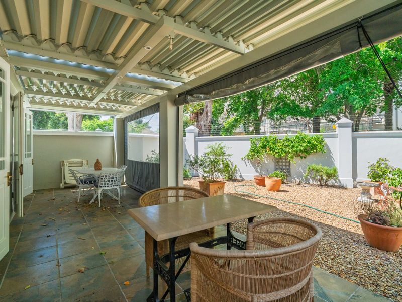 A covered patio area featuring tiled flooring, a corrugated roof, and retractable blinds, overlooking a low-maintenance gravel garden with a perimeter wall.