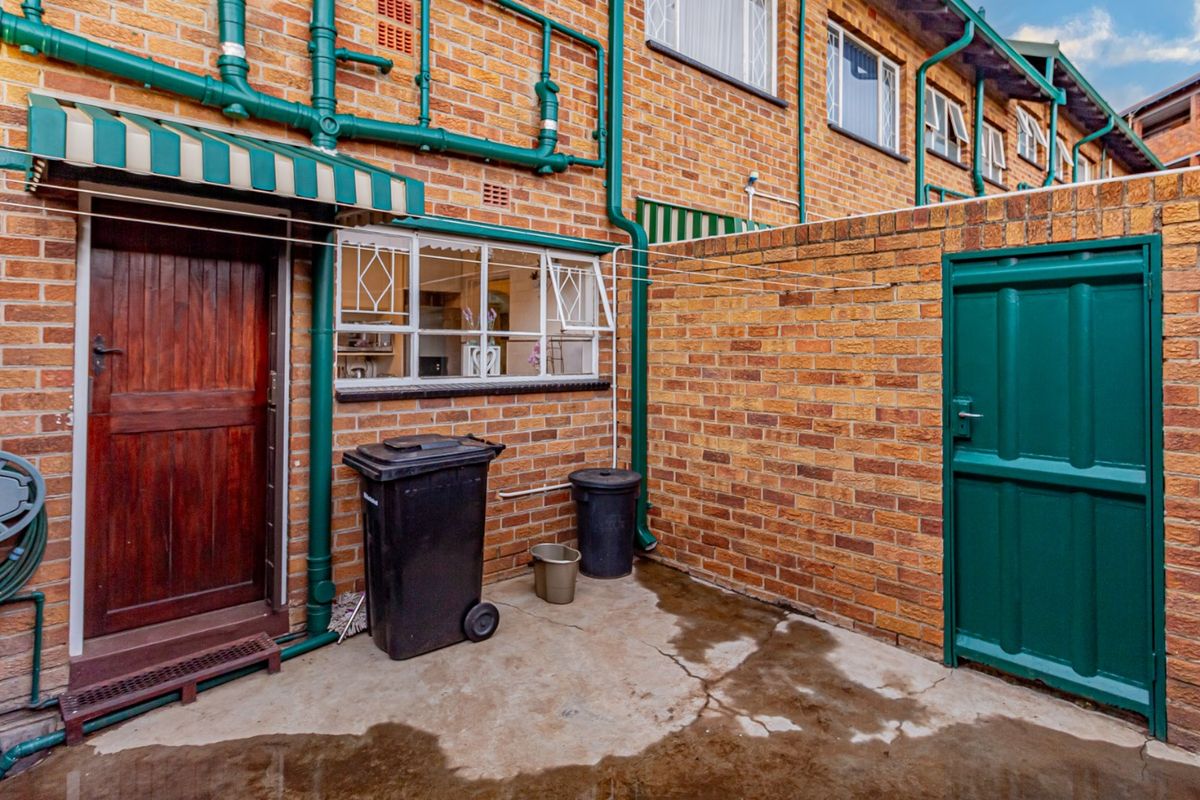 A functional rear courtyard area featuring exposed brick walls, external plumbing, a small awning, and a secure gated entrance.