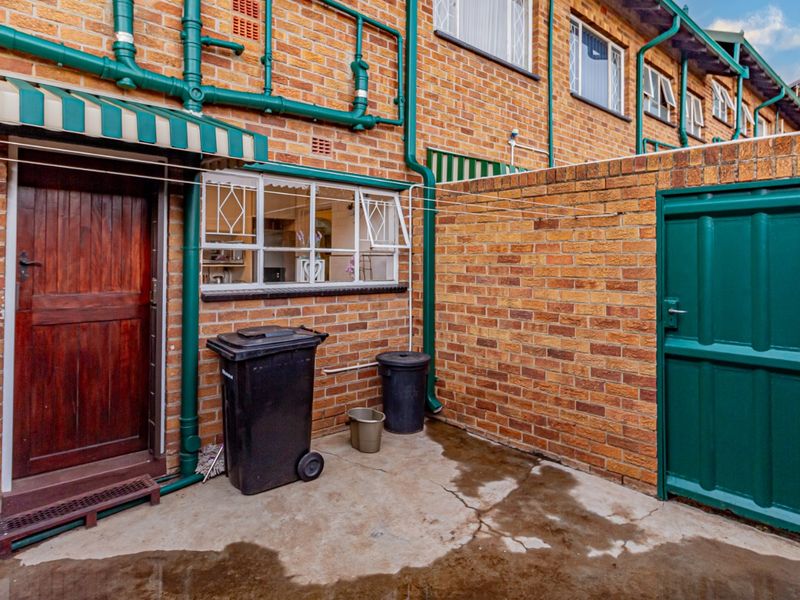 A functional rear courtyard area featuring exposed brick walls, external plumbing, a small awning, and a secure gated entrance.