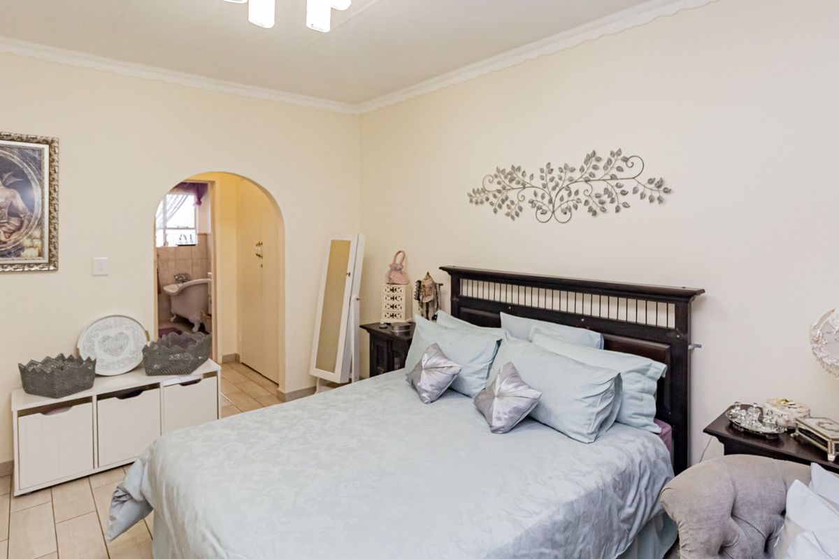 A bedroom featuring tiled flooring, a coved ceiling, and an arched doorway leading to an en-suite bathroom.