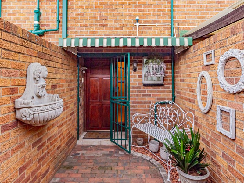 A private entrance area featuring brick walls, paved flooring, a wall-mounted fountain, and a secure timber door with a metal security gate.