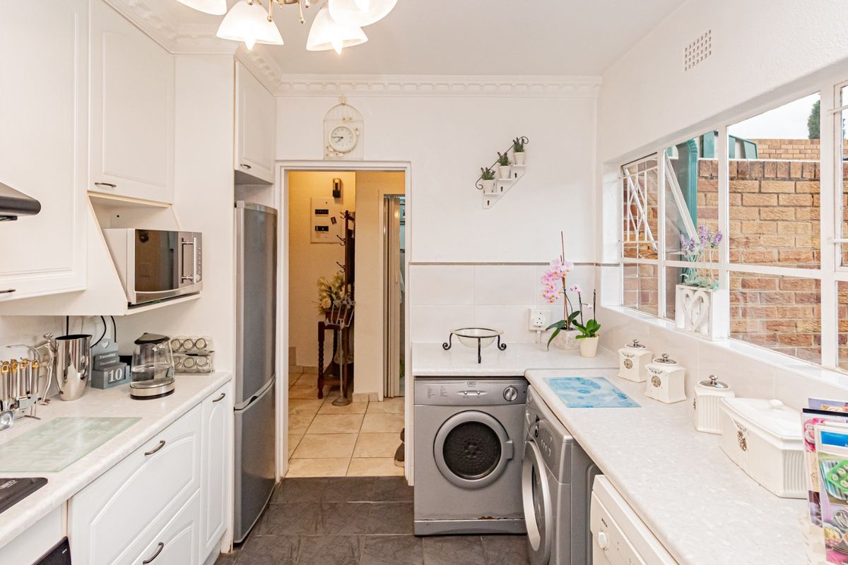 A functional kitchen featuring white cabinetry, laminate countertops, integrated appliances, and tiled flooring with natural light from a side window.