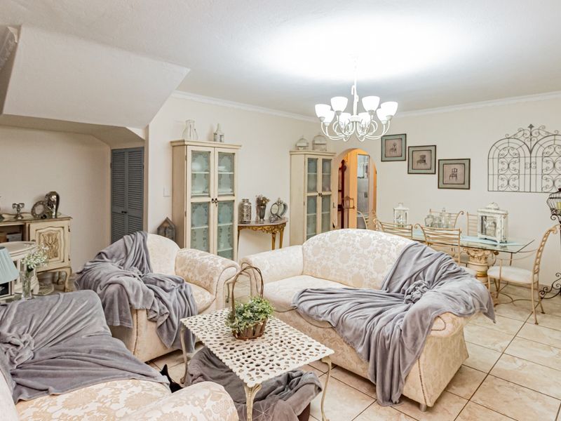 Spacious open-plan living and dining area featuring neutral tiled flooring, classic chandelier lighting, and built-in cabinetry, offering a versatile layout for comfortable family living.
