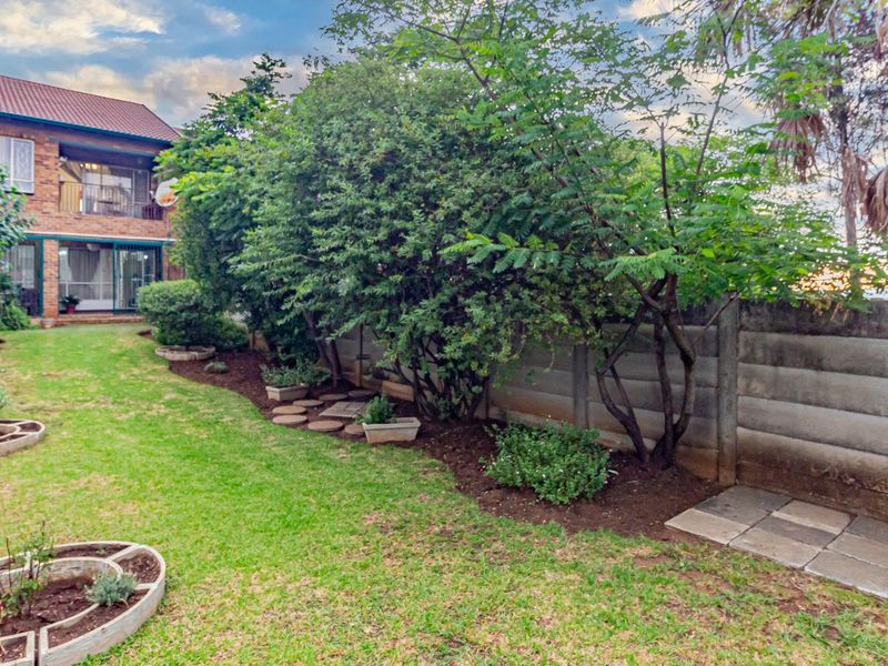 A private rear garden featuring a well-maintained lawn, established trees, landscaped garden beds, and a secure precast concrete boundary wall.