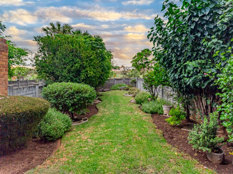 A private rear garden featuring a central lawn area bordered by established shrubs, trees, and a combination of brick and precast concrete boundary walls.