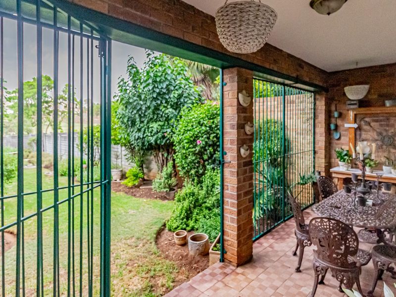A covered patio area featuring brick walls and tiled flooring, providing direct access to the garden through secure metal gates.