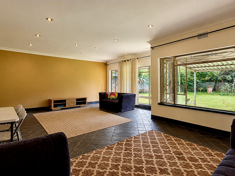 Spacious living room featuring tiled flooring, recessed lighting, and large windows providing natural light and access to the rear garden.